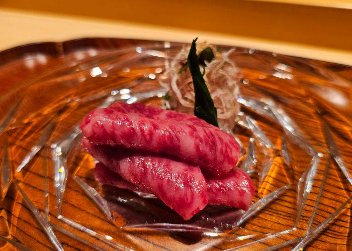 Three slices of beef sashimi, gently folded to highlight their delicate marbling.